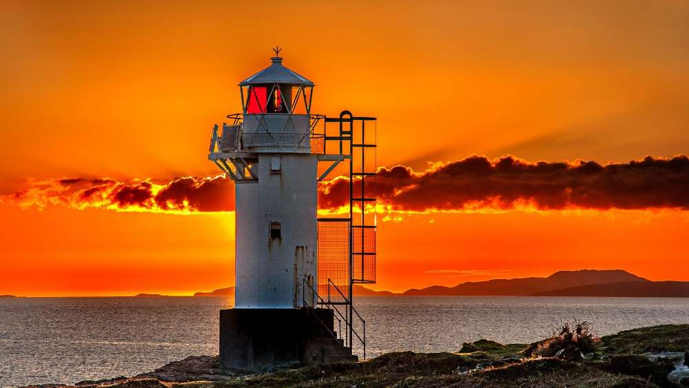 Lighthouse against Fiery Sunset Skies wallpaper