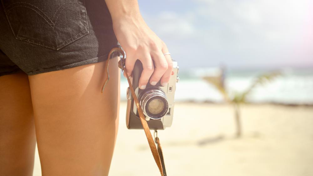 Girl Holding Camera on Sunny Beach wallpaper