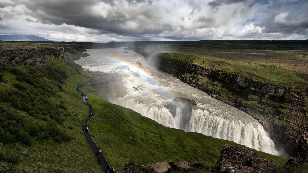 Majestic Waterfall Amidst Lush Greenery and Rainbows wallpaper