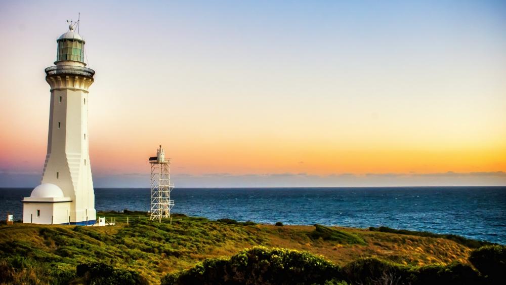 Serene Lighthouse at Sunset Overlooking Tranquil Waters wallpaper