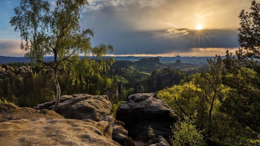 Serene Sunset Over Rocky Landscape with Lush Greenery wallpaper