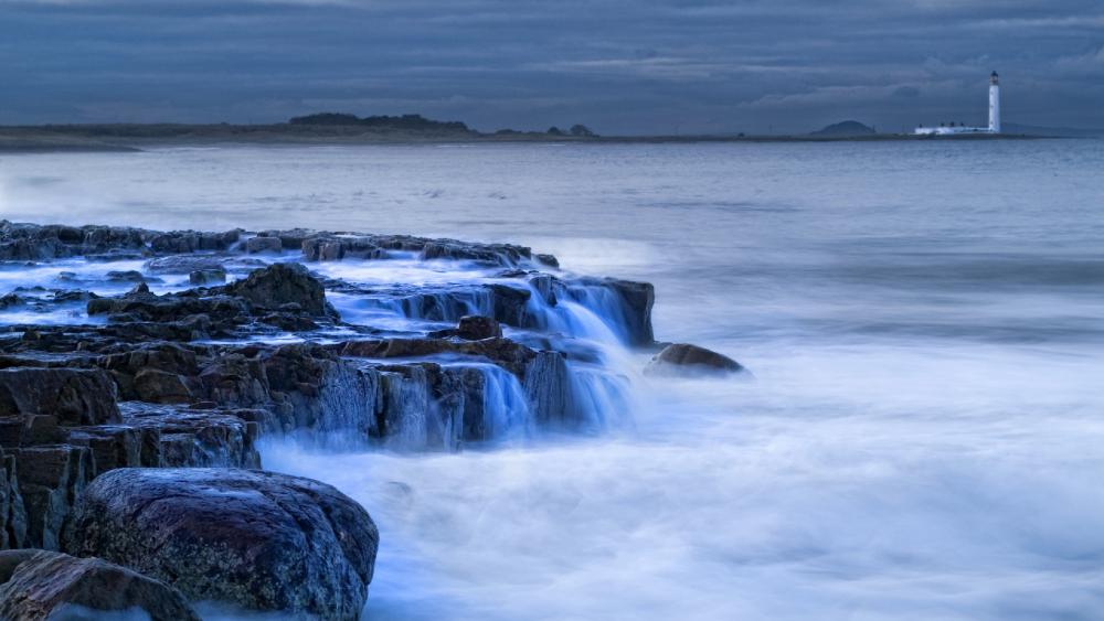 Serene Coastal View with Lighthouse and Gentle Waves wallpaper
