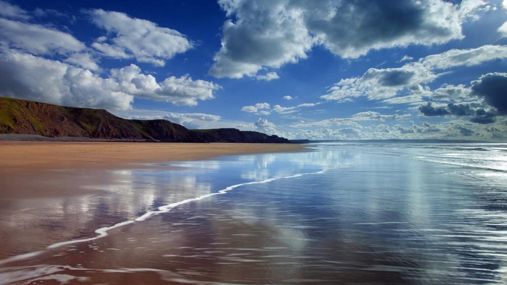 Serene Coastal Landscape Under Blue Skies with Waves wallpaper