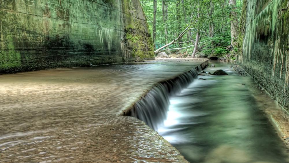 Serene Forest Stream Flowing Through Stone Passage wallpaper