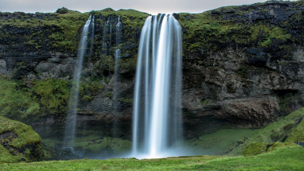 Majestic Waterfall Cascading Down Rocky Cliffs wallpaper