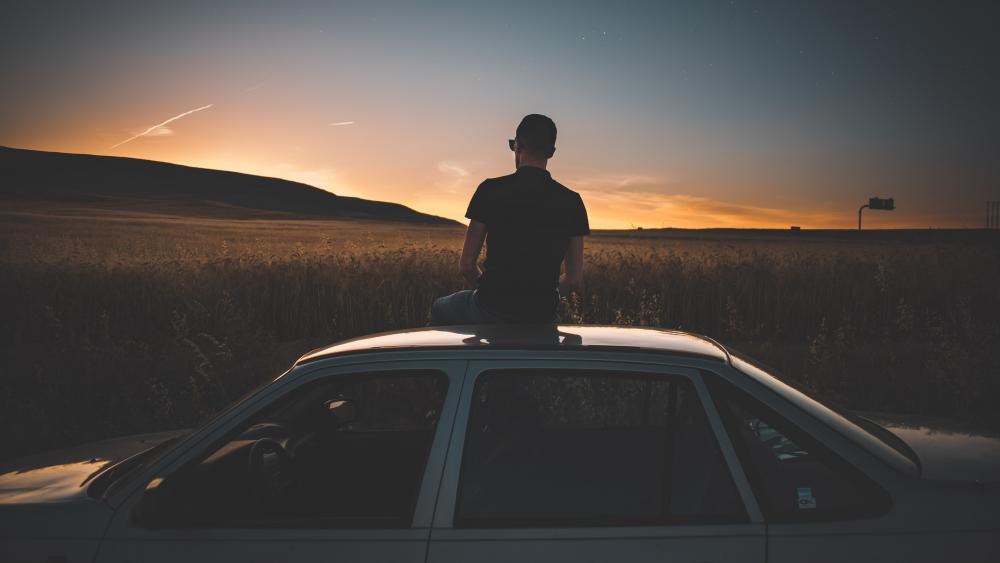 Guy sitting on top of car watching sunset wallpaper