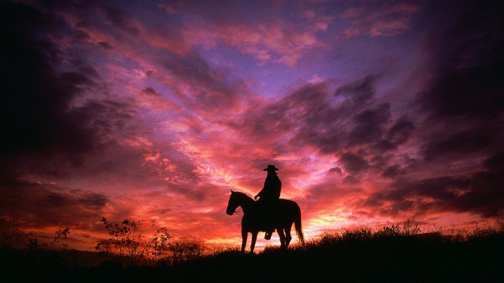 Cowboy Silhouette Against a Vivid Sunset Sky wallpaper