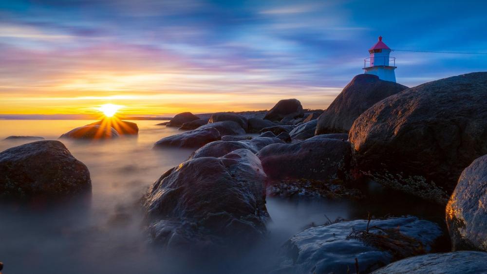 Serene Sunset by the Lighthouse on Rocky Shoreline wallpaper