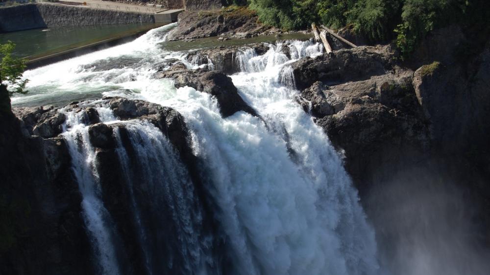 Majestic Waterfall Cascading Down Rocks Amidst Lush Greenery wallpaper
