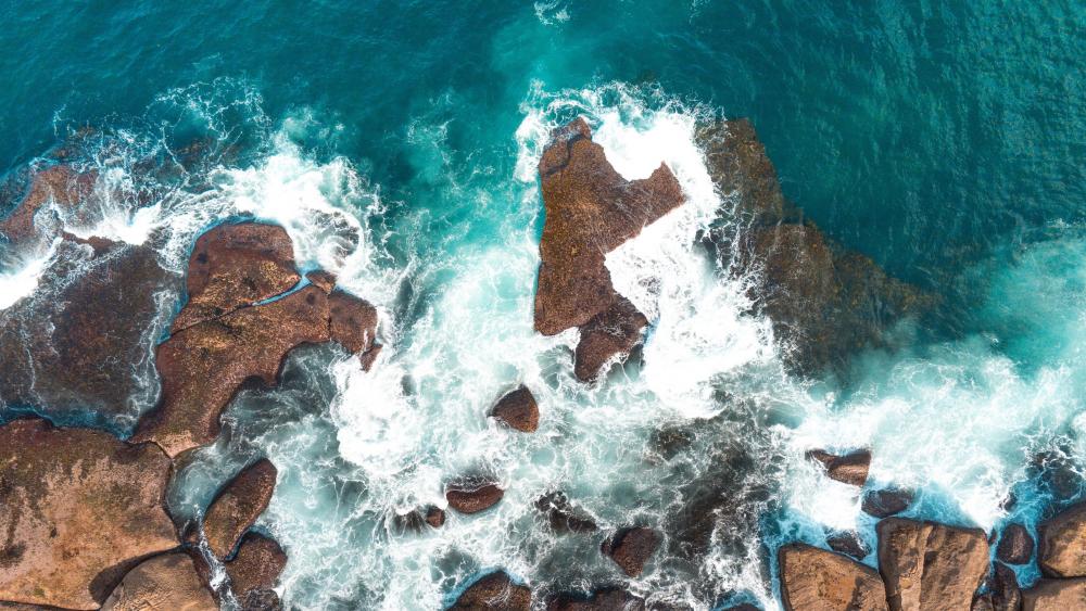 Turquoise Waters Clashing Against Rocky Shores wallpaper