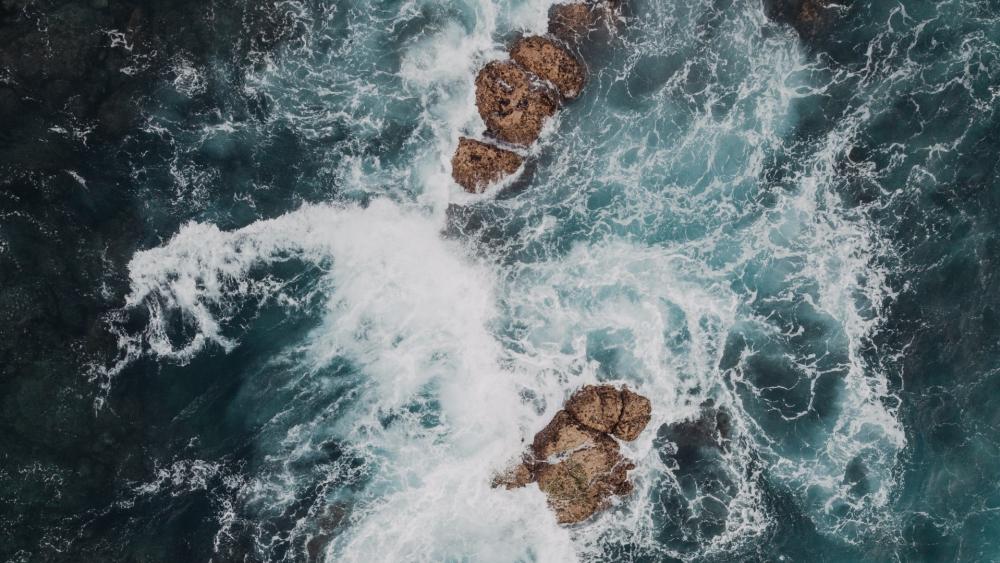 Waves Crashing Over Rugged Rocks in Turquoise Waters wallpaper