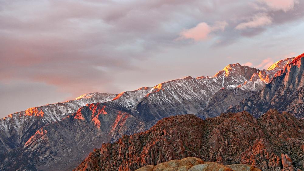 Sunlit Mountain Ridge Above Rugged Rocks and Snowy Summits wallpaper