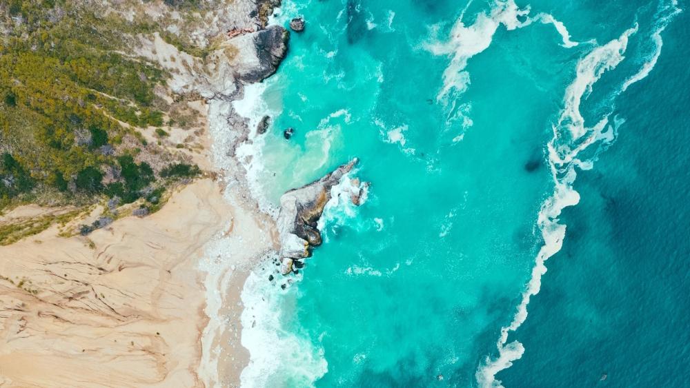 Turquoise Aerial Coastline Where Waves Brush Sand and Stone wallpaper