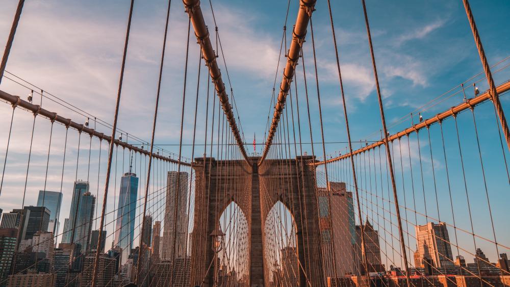 Sunlit Brooklyn Bridge Cables Framing Manhattan Skyline in New York City wallpaper