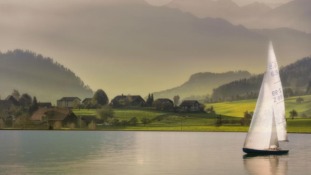 Sailboat Gliding Across Misty Valley Lake in Soft Morning Light wallpaper