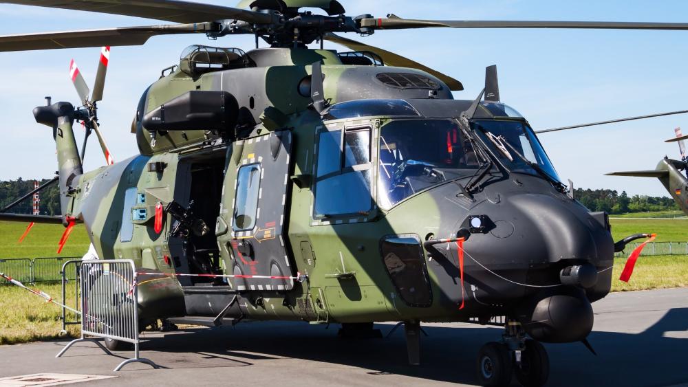 Camouflaged Military Helicopter on Airfield Tarmac Under Clear Blue Skies wallpaper