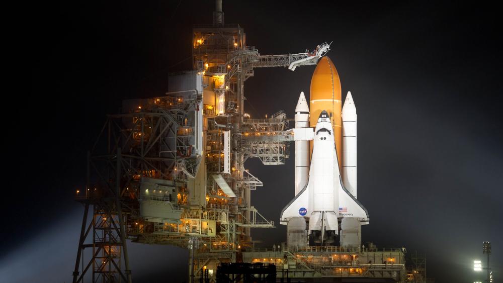 Space Shuttle and Launch Tower Lit Up Against the Night Sky wallpaper