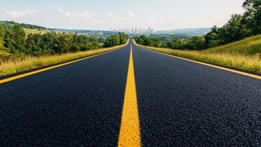 Endless Asphalt Highway Through Green Hills Toward Distant Skyline wallpaper
