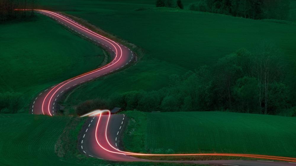 Winding Dusk Road Through Rolling Green Hills With Light Trails wallpaper