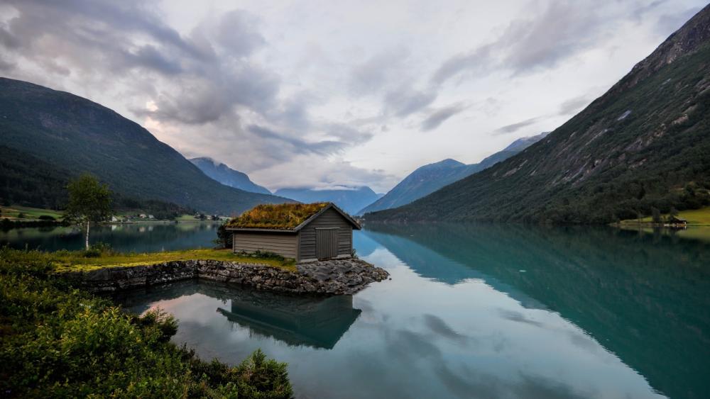 Grass Roof Cabin Reflected in a Quiet Norwegian Fjord Valley wallpaper