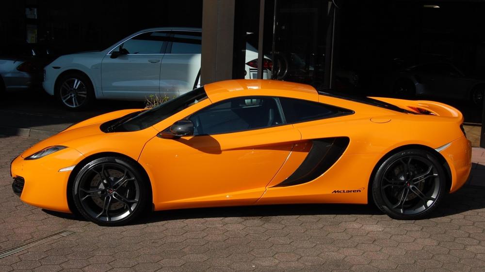 Sunlit Orange McLaren Coupe Profile in Urban Showroom Shadow wallpaper