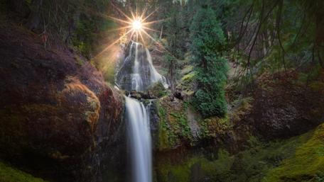 Stunning Waterfall Surrounded by Lush Greenery and Sunlight wallpaper