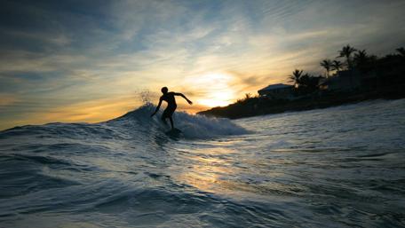 Surfing at Sunset Shows Thrilling Ocean Adventure wallpaper