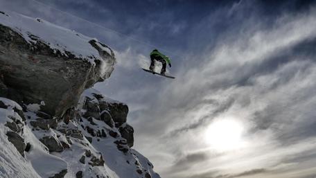 Thrilling Snowboard Leap Amidst Majestic Mountains wallpaper