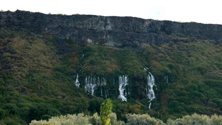 Serene Waterfalls Behind Lush Greenery wallpaper