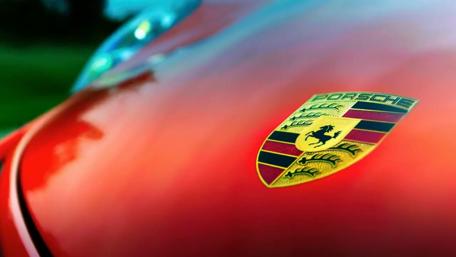Iconic Porsche Emblem on Vibrant Red Car Surface wallpaper