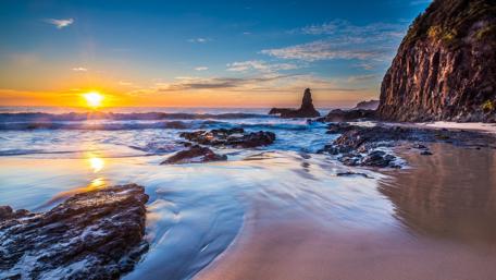 Sunset Serenity: Waves Against Rocky Shores wallpaper