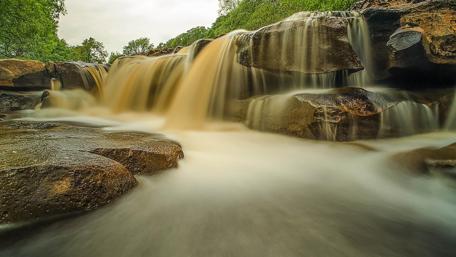 Serene Waterfall Setting Amidst Stones and Lush Greenery wallpaper