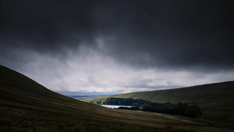 Dark Clouds Over Rolling Hills and Lake Scene wallpaper