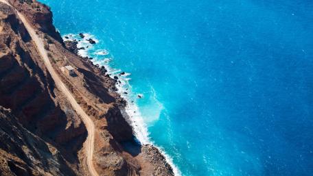 Serene Coastal View of Rocky Seashore Amidst Vibrant Blue Waters wallpaper
