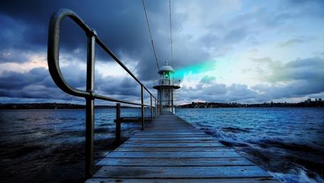 Lighthouse-Illuminated Pier Under Cloudy Sky wallpaper