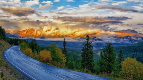 Winding Road Through Autumn Forest and Clouds wallpaper