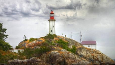 Lighthouse on Rocky Coastline in Cloudy Skies wallpaper