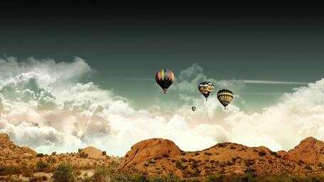 Colorful Hot Air Balloons Soar Above Mountains and Clouds wallpaper