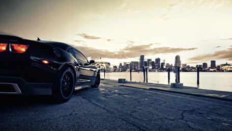 Sleek Black Car Against Urban Skyline at Dusk wallpaper