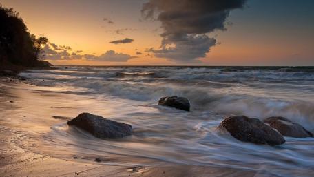 Serene Sunset Over Waves and Stones wallpaper