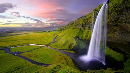 Majestic Waterfall at Sunset Over Green Fields wallpaper