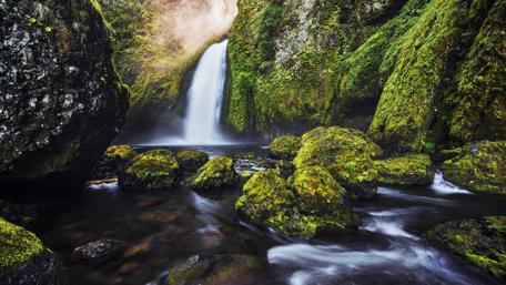 Serene Waterfall Amidst Lush Greenery and Stones wallpaper