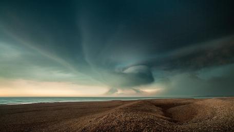 Dramatic Storm Clouds Over Tranquil Shoreline wallpaper