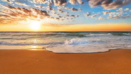 Sandy beach with foamy waves at sunset wallpaper