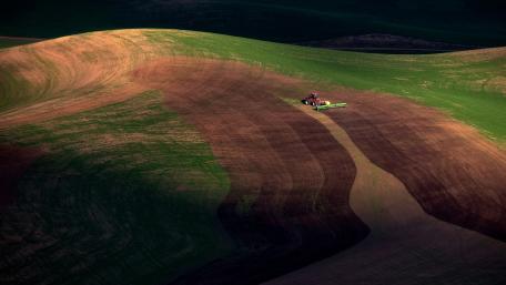 Tractor Tending to Rolling Hills in Vibrant Landscape wallpaper