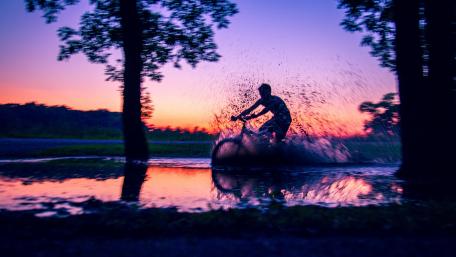 Cyclist Splashing Through Water at Sunset wallpaper