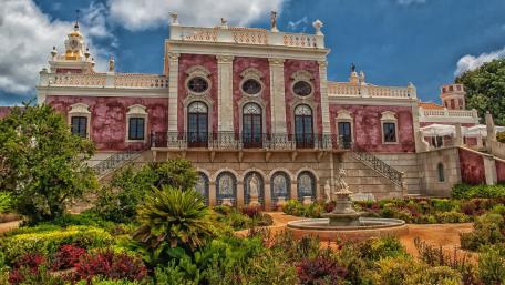 Elegant Castle Surrounded by Lush Gardens and Blue Sky wallpaper