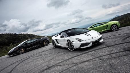 Ultimate Sports Car Trio Displayed on Scenic Road wallpaper