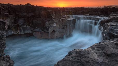 Majestic Waterfall at Sunset Over Rocky Terrain wallpaper