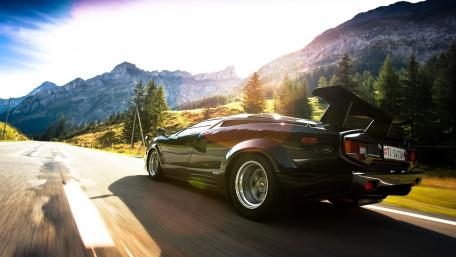 Sleek Black Sports Car on Open Road Under Mountains wallpaper